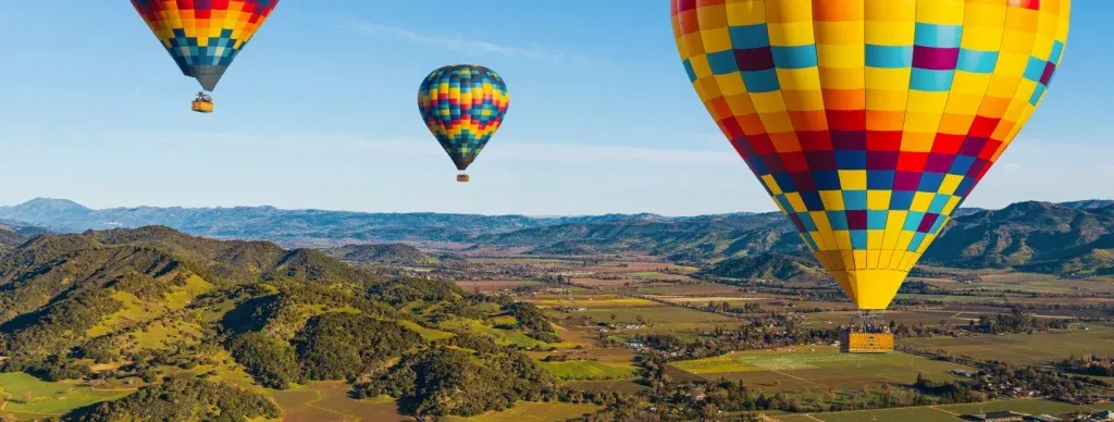 Hot air balloons from Napa Valley Aloft floating above vineyard rows at sunrise over Napa Valley, California